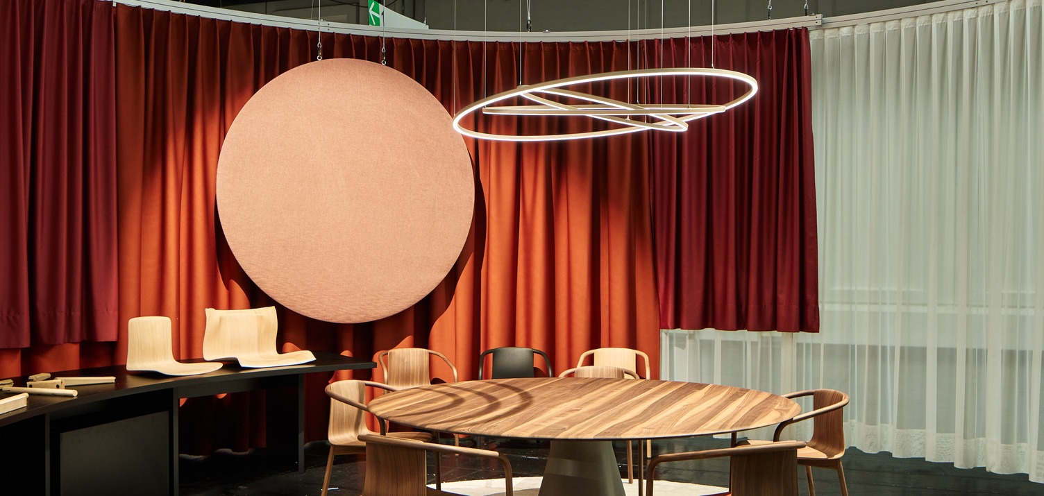 ORGATEC 2024 - WALTER KNOLL - PURE MOTION Tischsitzgruppe aus Holz von WALTER KNOLL über der eine Lichtskulptur bestehend aus drei leuchtenden Ringen abgependelt ist.