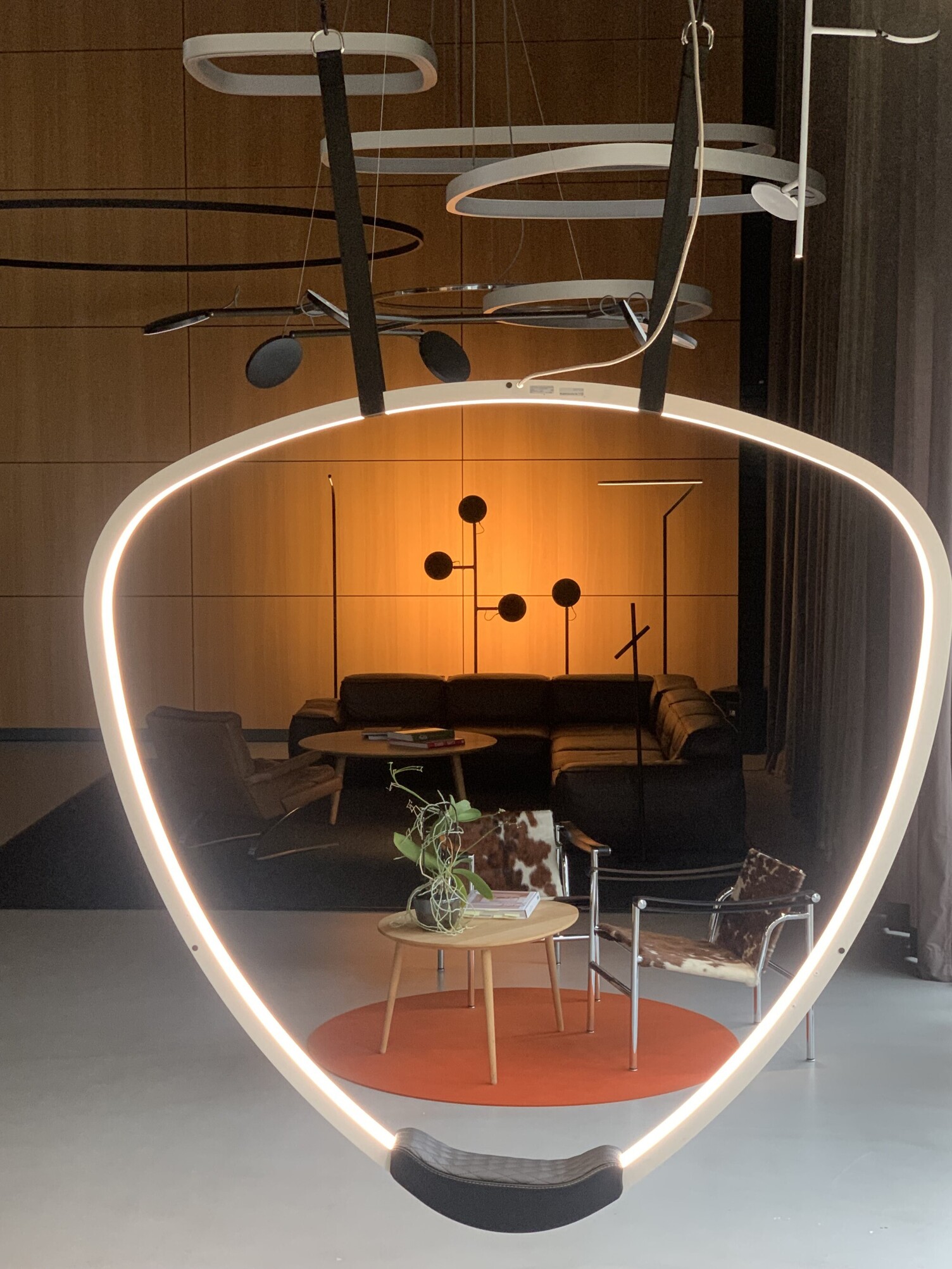 SATTLER Stehleuchtenensamble Leuchten-Showroom Sattler, Blick durch die dreieckige SOFT-DELTA-Lichtschaukel auf die Stehleuchten: AVVENI Floor, PALITO Floor, Fino Floor und Insospeso Floor.
