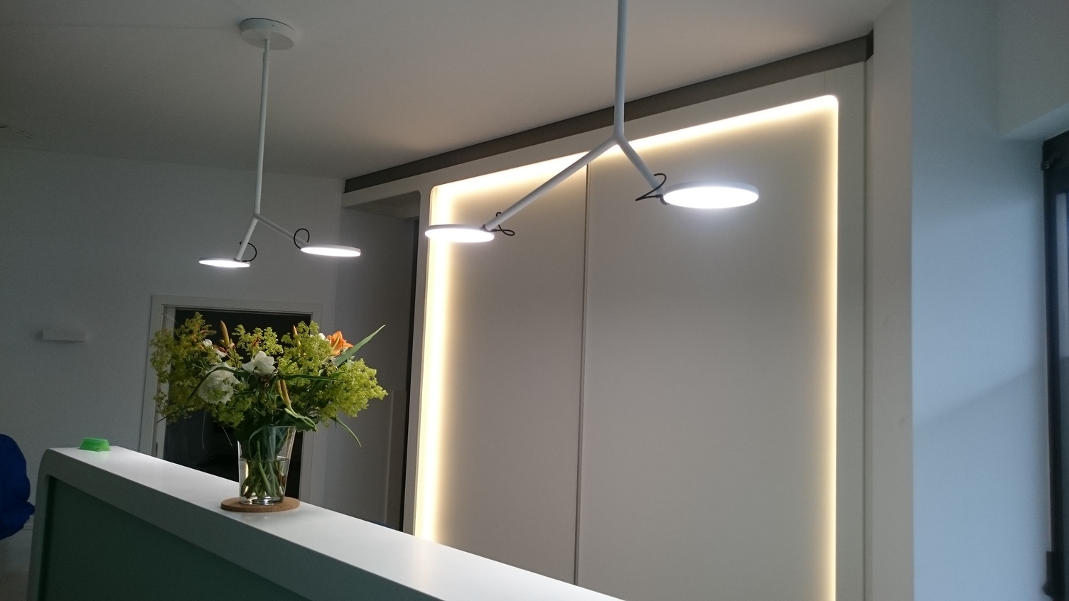 Empfangstheke mit zwei verzweigten Anbauleuchten AVVENI CEILING 2 Weiße Empfangstheke mit zwei weißen einfach verzweigten Anbauleuchten AVVENI CEILING 2. Jede Leuchte endet in zwei beweglichen runden flachen Leuchtenköpfe.