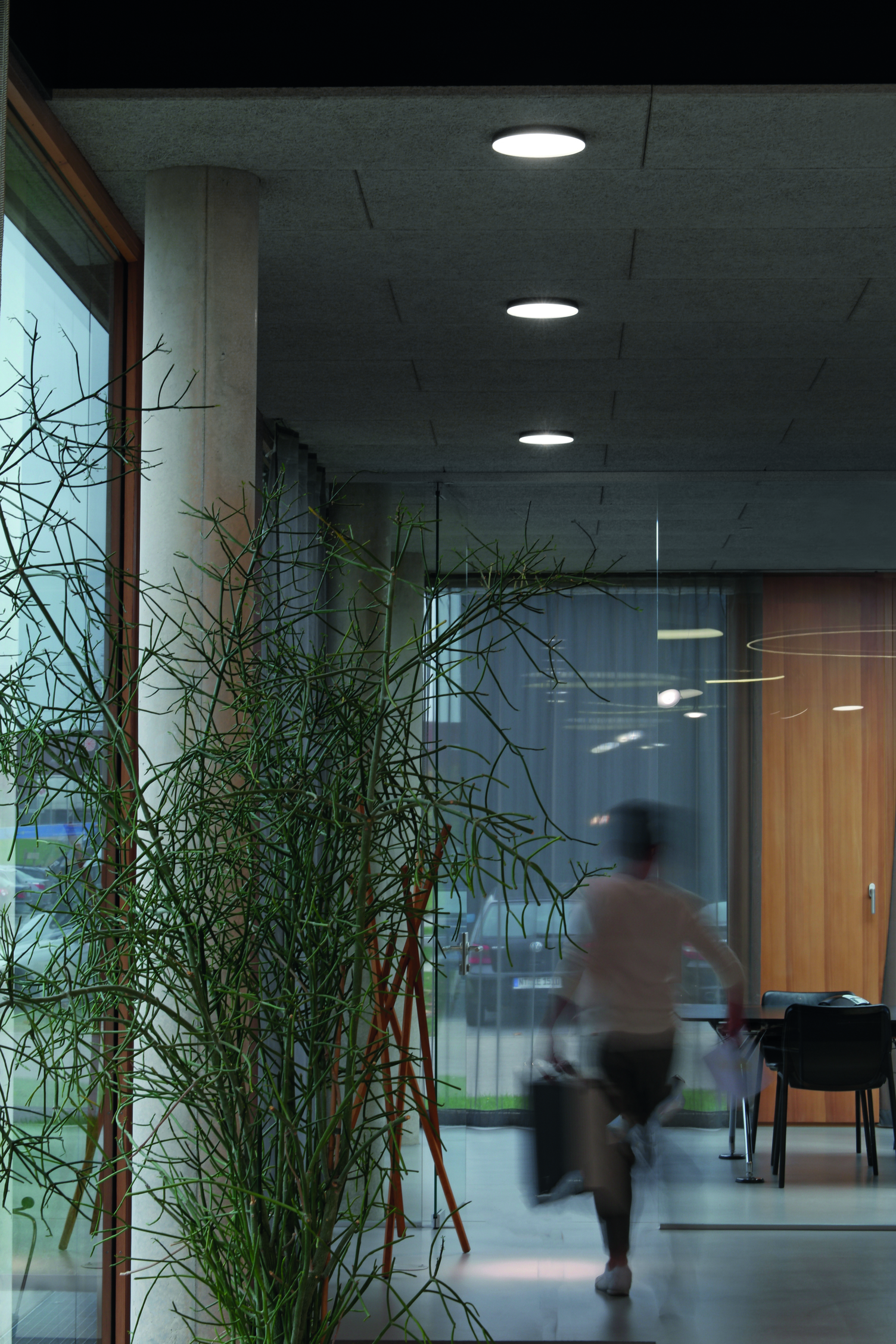 Gehende Person auf dem Flurweg in den Besprechungsraum unter drei flachen, runden Halbeinbau-Spots AVVENI PURE mit schwarzem Rand.