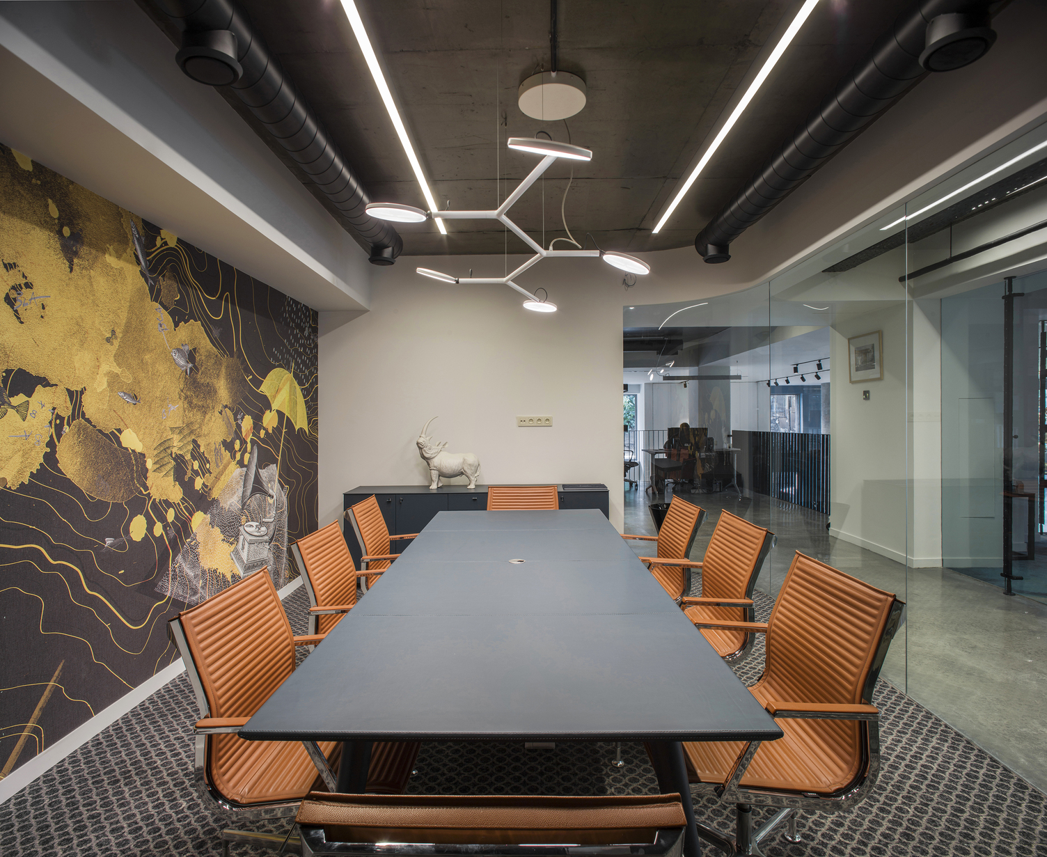 Modern meeting room with orange chairs and a white branched luminaire with 5 round flat lamp heads (AVVENI PENDANT 5) above the long black table.