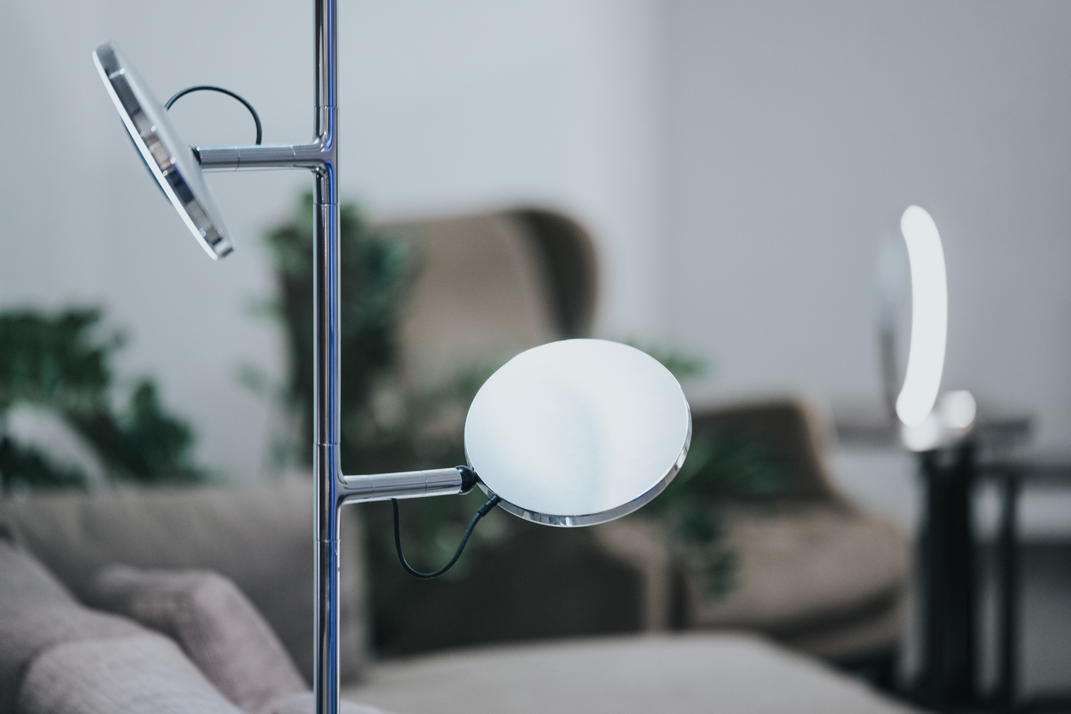 AVVENI FLOOR 3 in Aluminium poliert Ausschnitt einer Stehleuchte in Aluminium poliert mit flachen, runden Leuchtenköpfen AVVENI Floor 3 vor Sofa-Möbeln, im Hintergrund Tischleuchtenring SLIM TABLE.