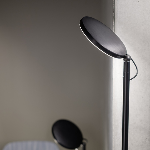 Two black floor lamps from the AVVENI FlOOR series of different heights with a round, flat lamp head at the side of a table and blue chair from the Brunner Group.