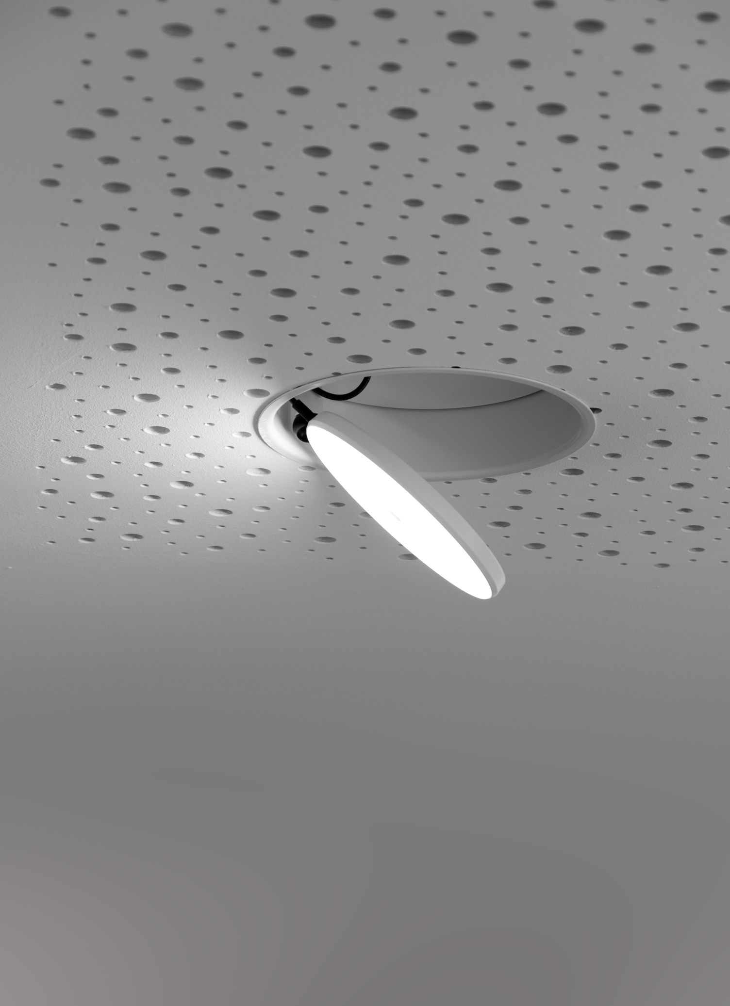White round, flat, fold-out and rotatable semi-recessed AVVENI downlight with frame in white perforated ceiling.