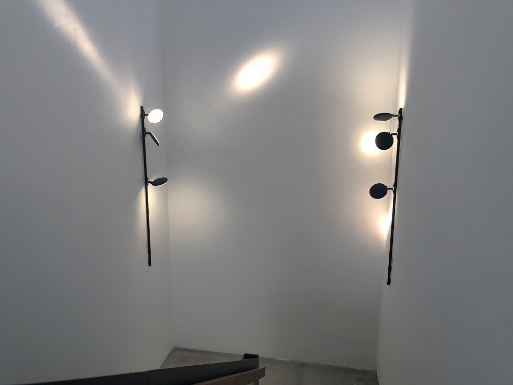 Wandanbau Stromschienensystem lightlight+AVVENI im Treppenhaus Weißes Treppenhaus, mit zwei schwarzen Wandanbau Stromschienensystemen lightlight + 2 flexiblen Leuchtenköpfen AVVENI, links und rechts auf Höhe des Treppen-Wendepodest.