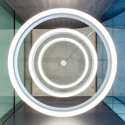Glass tower with outwardly illuminated CIRCOLO INVERSE ring luminaires View from below of three large ring luminaires radiating outwards, CIRCOLO INVERSE with a diameter of 1.32 metres, suspended one below the other in a glass tower.
