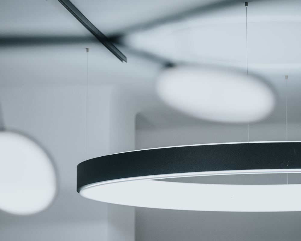 CIRCOLO L-Version Bild mit schwarzer Ringleuchte im Fokus im Hintergrund und verzweigter schwarzer Pendelleuchte mit in verschiedene Richtungen ausgerichtete runde Leuchtenköpfen (AVVENI) unscharf im Vordergrund.