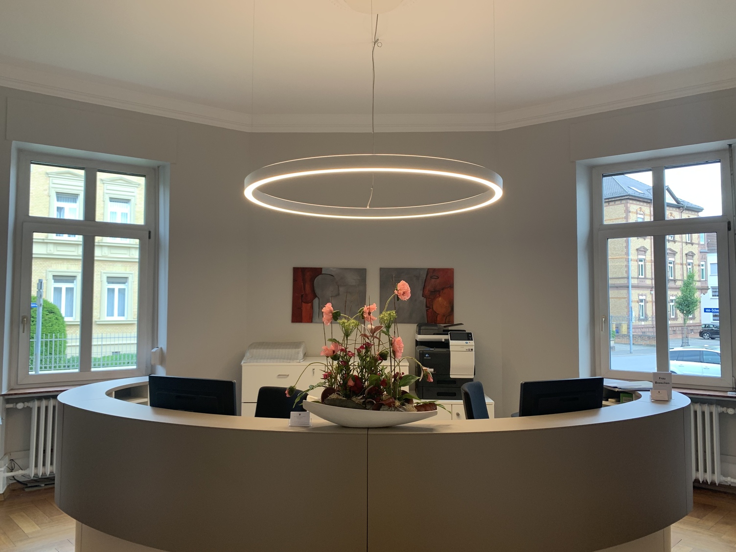 Runde Empfangstheke in einem kleinen Büro, über den Arbeitsplätzen ist eine Ringleuchte (DUETTO) abgependelt.