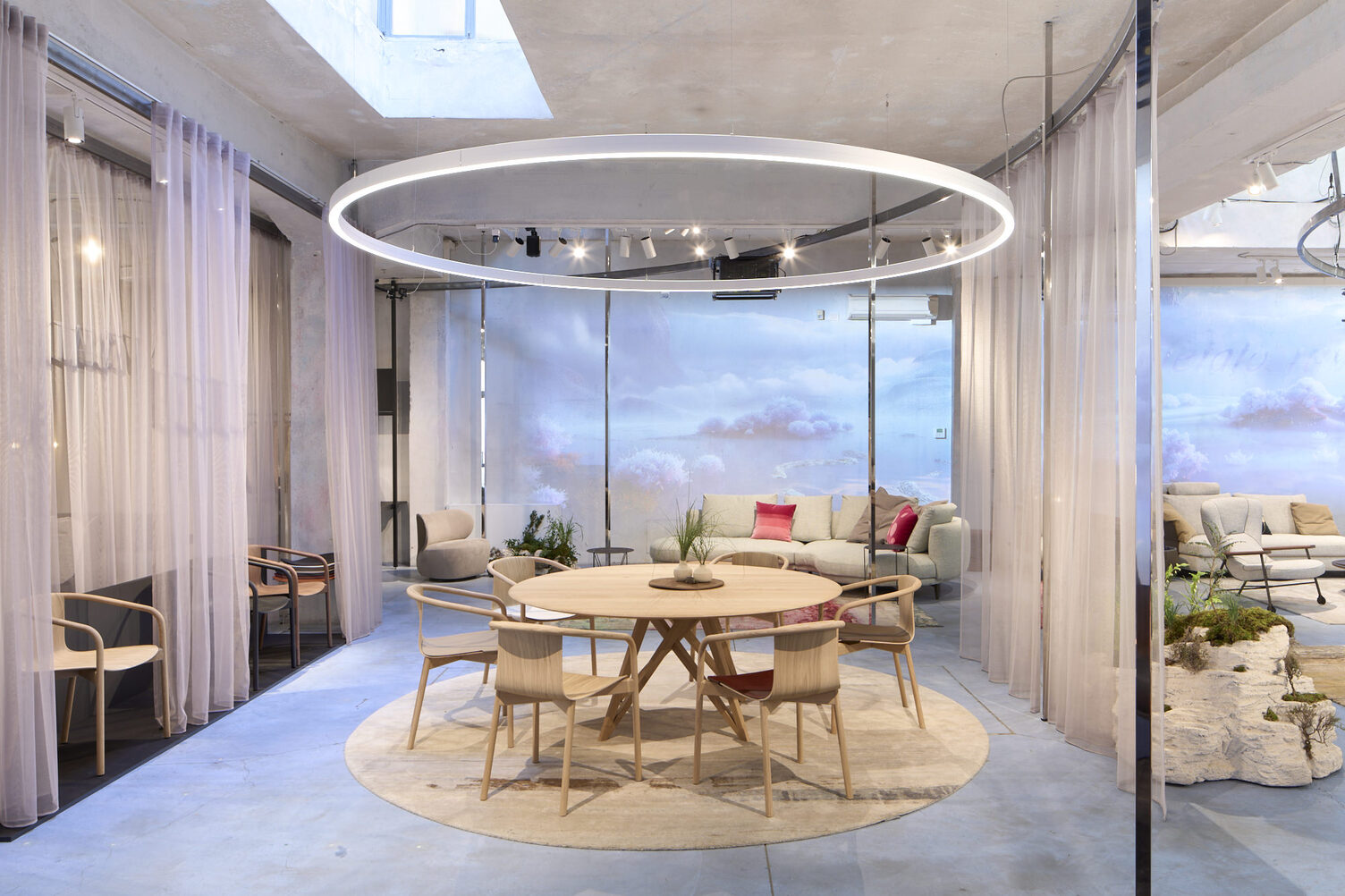 Messestand Walter Knoll, Messe Mailand, Designweek 2024 Messestand mit Wolkenwänden, Vorhängen und zentral im Fokus durch eine runde Ringleuchte (DUETTO) in Szene gesetzt ist eine Esstischgruppe mit Stühlen von WALTER KNOLL.
