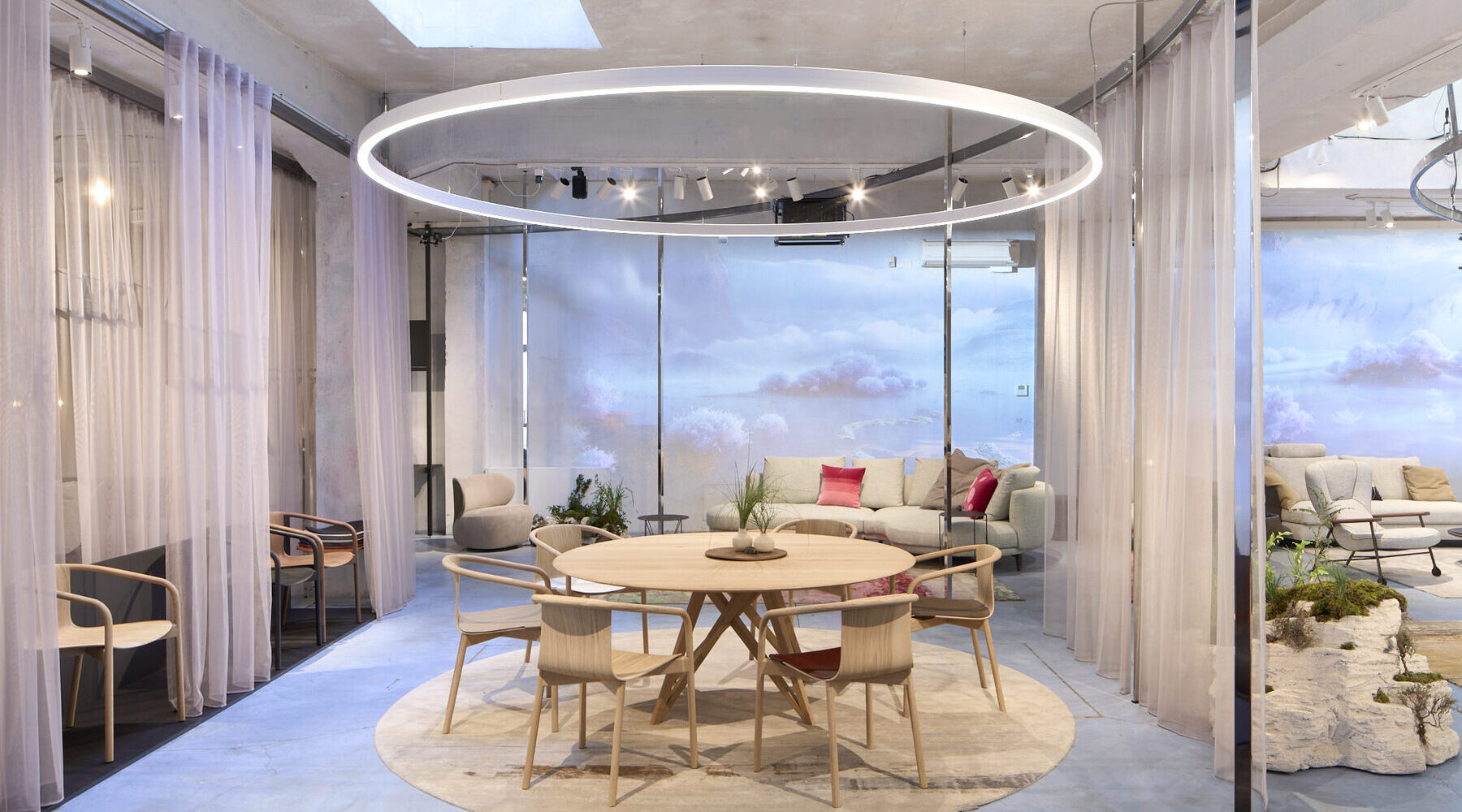 Messestand Walter Knoll, Messe Mailand, Designweek 2024 Messestand mit Wolkenwänden, Vorhängen und zentral im Fokus durch eine runde Ringleuchte (DUETTO) in Szene gesetzt ist eine Esstischgruppe mit Stühlen von WALTER KNOLL.
