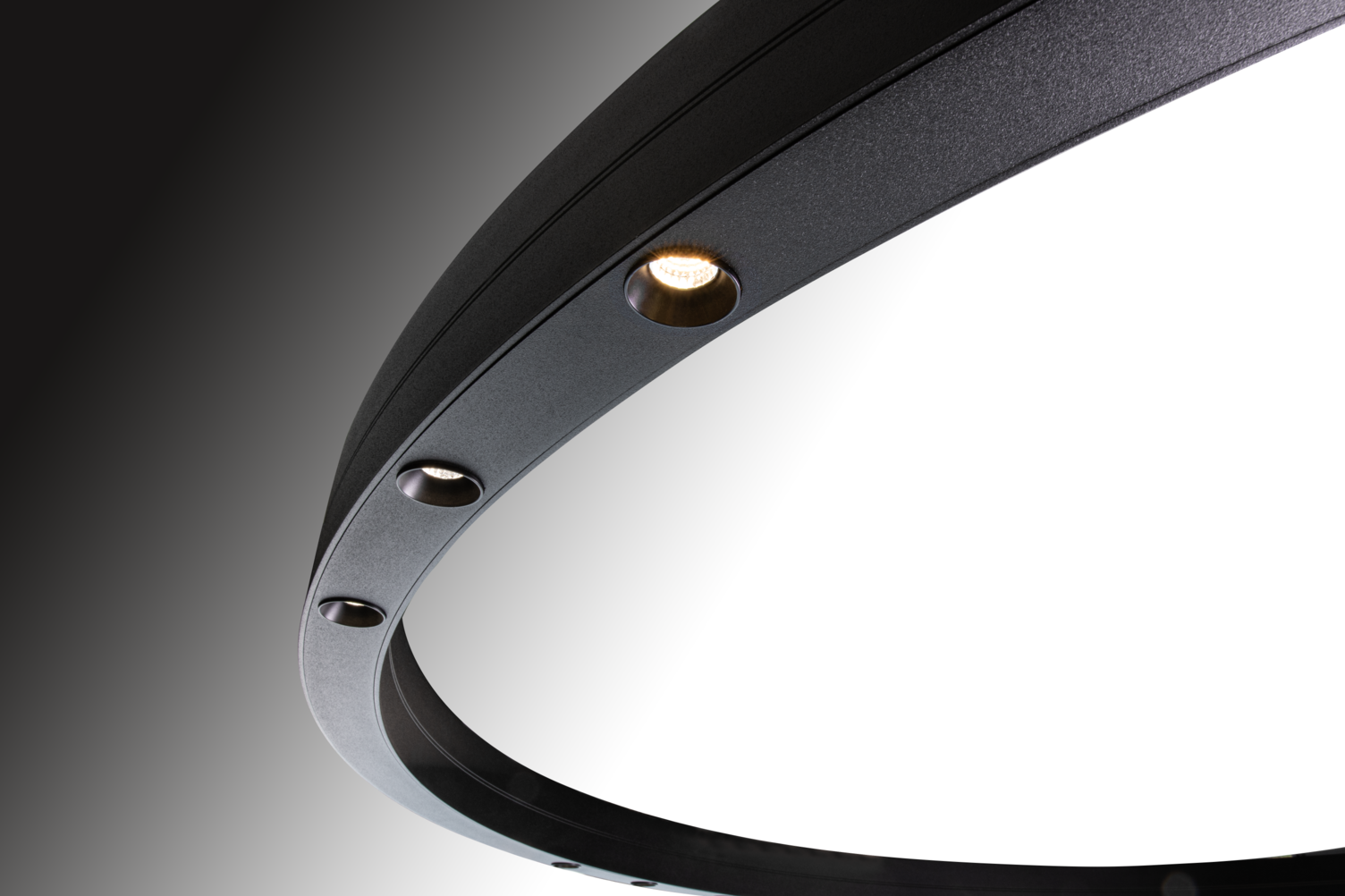 Gruppenweise angeordnete runde Linsen Ausschnitt einer schwarzen Ringleuchte, DUETTO LENS, sichtbar sind drei runde leuchtende Linsen mittig im Ringprofil direkt leuchtend.