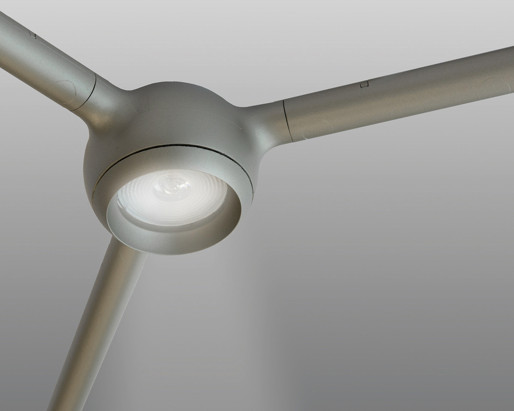 direct light (24° lens) Front of the light head of the FAVO CELL luminaire's mesh structure as a node with three symmetrically extending arms in sand silver finish, with a large round lens for direct light in the centre of the light head.