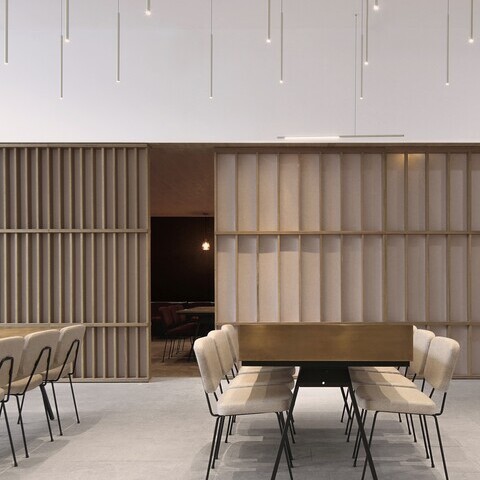 Lighting for the Altarea Cogedim lounge area, Paris | FINO pendant lights Lighting in the lounge area at Altarea Cogedim, Paris. Bright room with another seating area separated by light-coloured sliding partitions. Several FINO luminaires in warm champagne gold are suspended vertically above the tables in the foreground.