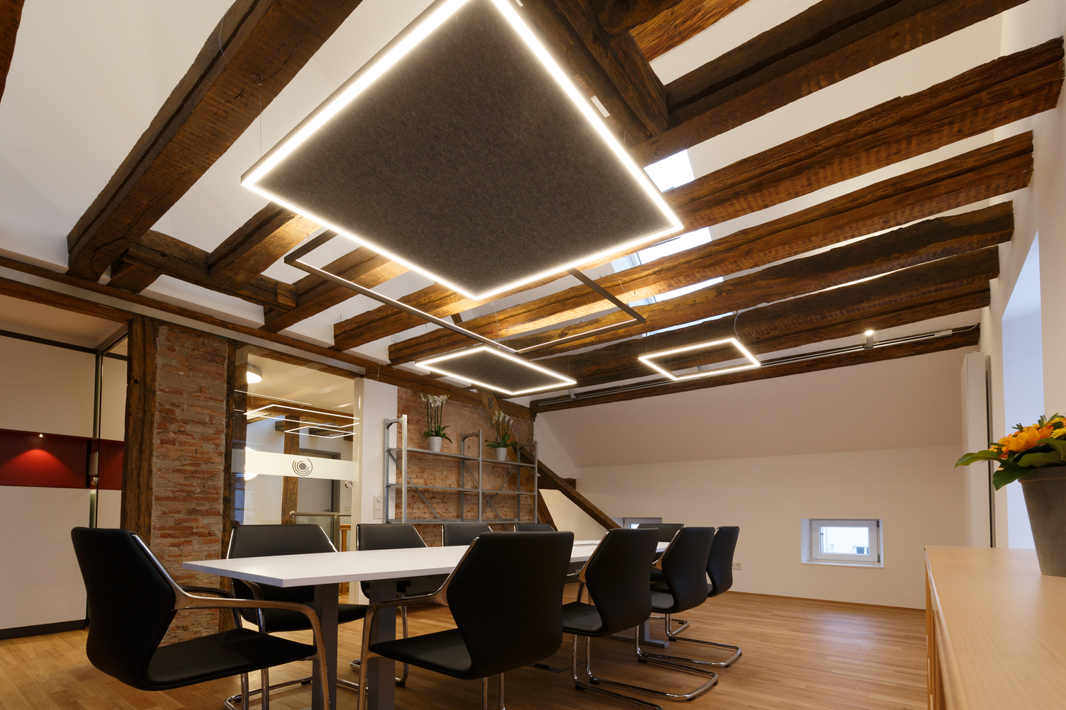 Meeting room with square GIOCO pendant luminaires | © Kiefer Raimund Warm meeting room with a rectangular meeting table with wooden beams on the ceiling and suspended luminaires in various square frame shapes, some fitted with felt acoustic absorbers. | © Kiefer Raimund