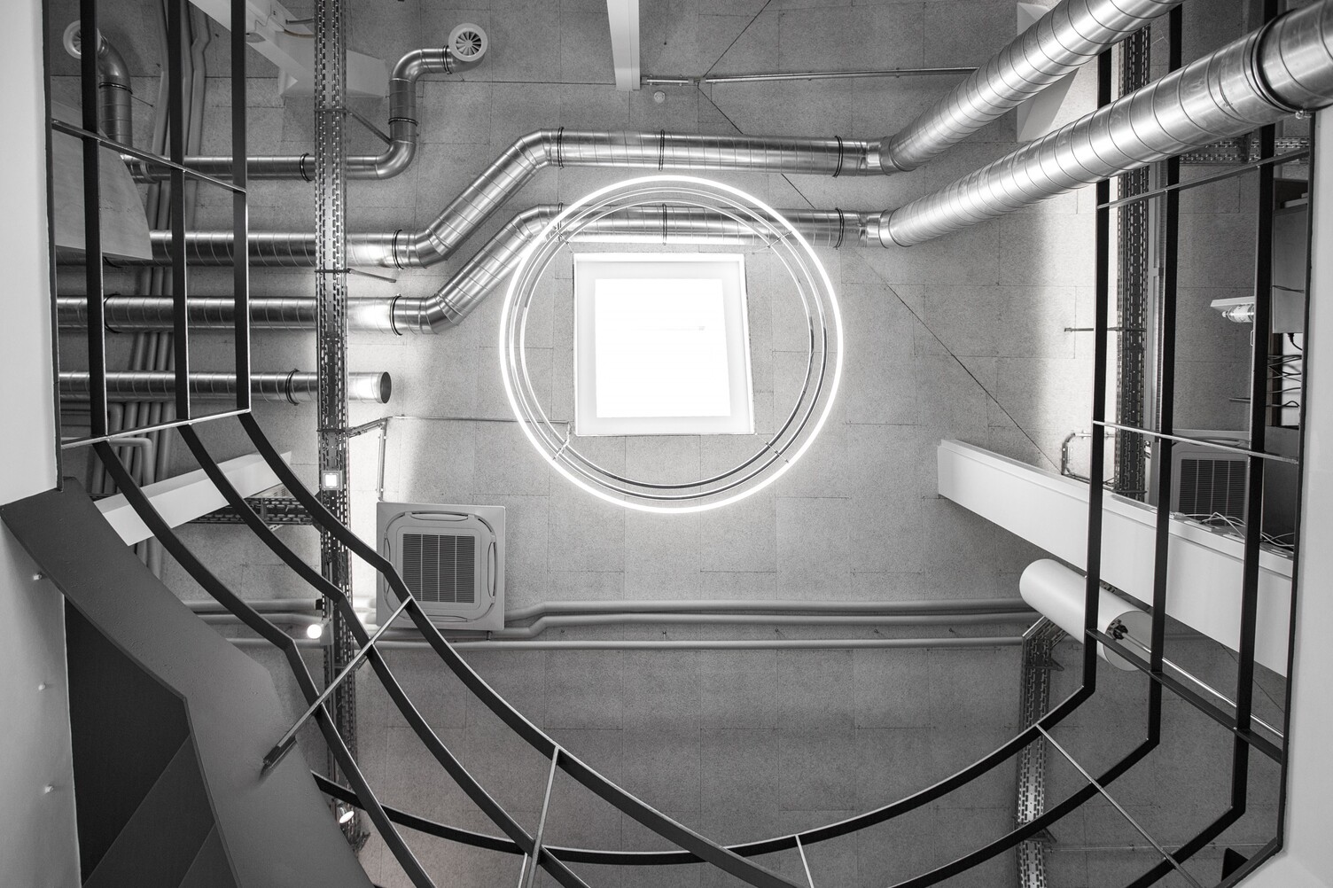 Kronleuchter INSIEME im Treppenauge eines Gebäudes im Industry Style Blick von unten in einem Treppenauge eines Beton-Industriegebäudes der madness GmbH an die Decke auf 3 untereinander hängende Ringleuchten der INSIEME.