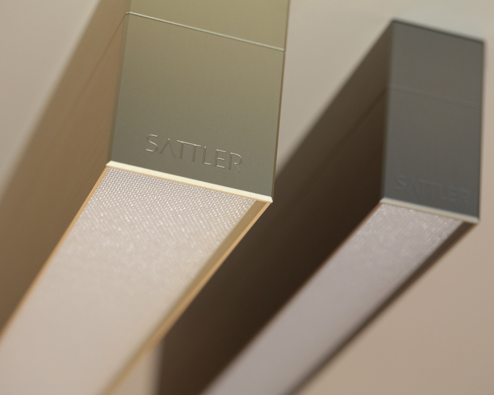 PALADIO PRISM profile sizes 54 mm and 35 mm Two aluminium linear lights photographed frontally from one end, the left one is champagne gold and slightly wider (PALADIO PRISM 54) than the right one in bronze (PALADIO PRISM 35), both are embossed with the lettering SATTLER.