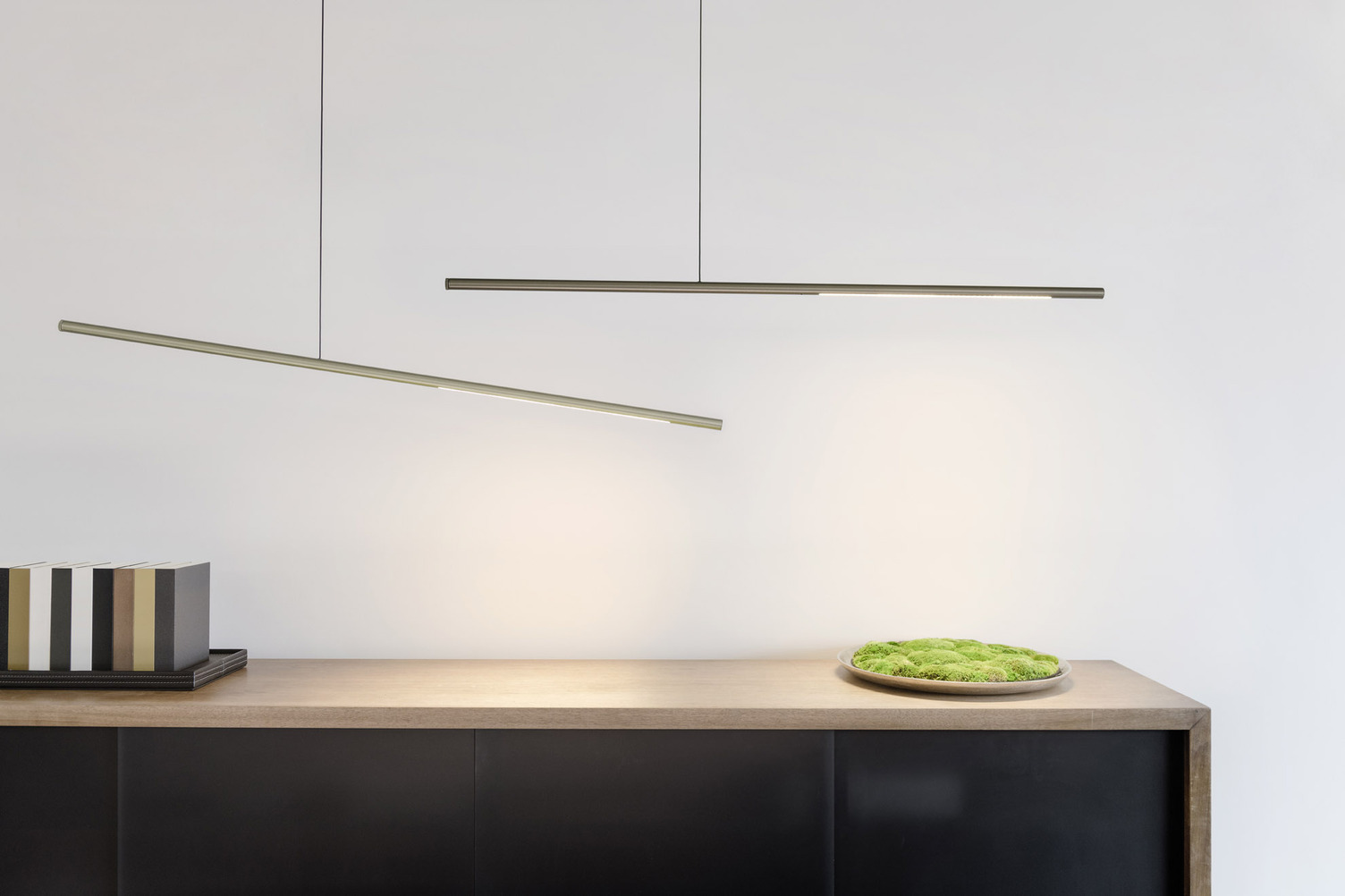 Theke mit zwei horizontalen Pendelleuchten PALITO Holztheke mit zwei darüber eher horizontal abgependelten Stableuchten der PALITO-Serie. Sie leuchten ein strahlend grünes Moosmuster an.