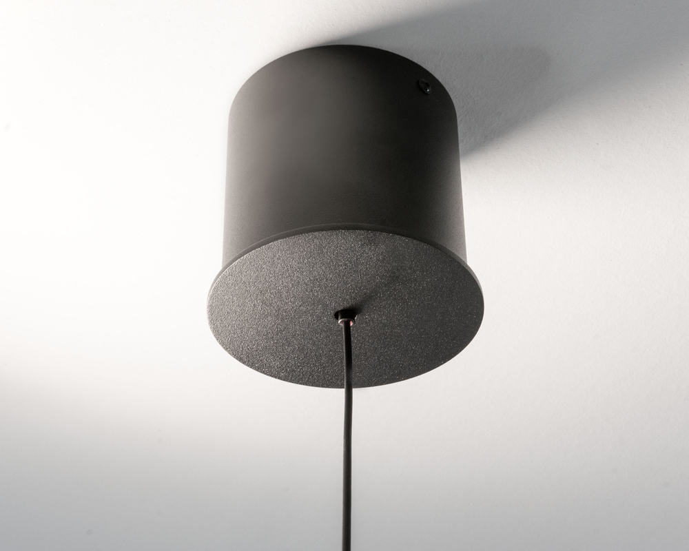 Black cylindrical ceiling canopy Light canopy of the PALITO, picture shows a short black cylinder on which a thin plate sits, the black cable is let out from the centre of this plate.