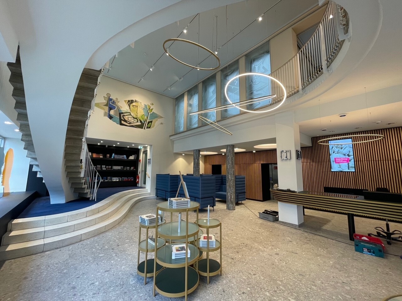 Multiple SLIM LED ring luminaires by SATTLER in custom gold powder-coated finish (068/90460), combining direct and indirect versions in various diameters, installed at Köln Tourismus in 2024.