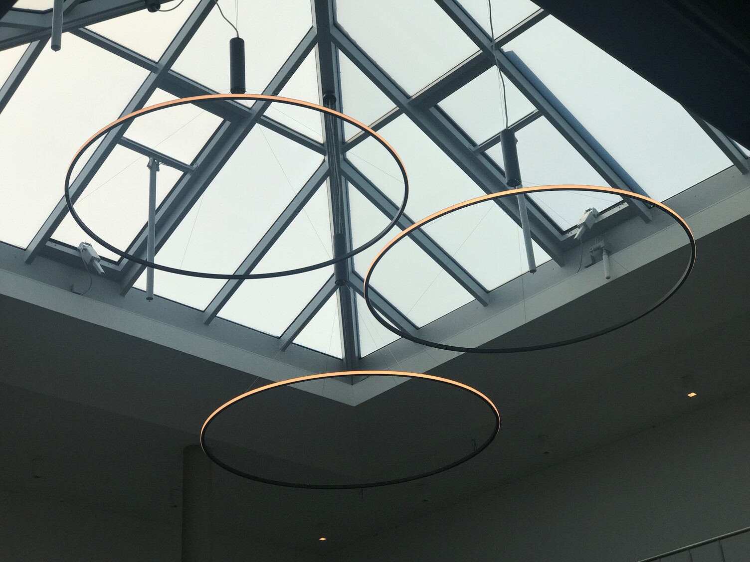 LED ring pendant light with pendant canopy (shining outwards) Pointed glass roof with three round ring pendant lights that shine towards the outside of the circle and are suspended from a cylindrical pendant canopy.