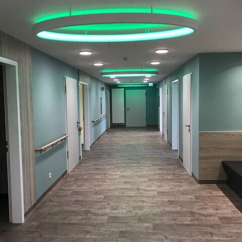 ELLIPSE as surface-mounted luminaire with ceiling spacer sleeves Corridor of the Paracelsus Clinic to the delivery room with green walls and many doors, large elliptical ring lights are attached to the ceiling through spacer sleeves, which light up in RGB green.
