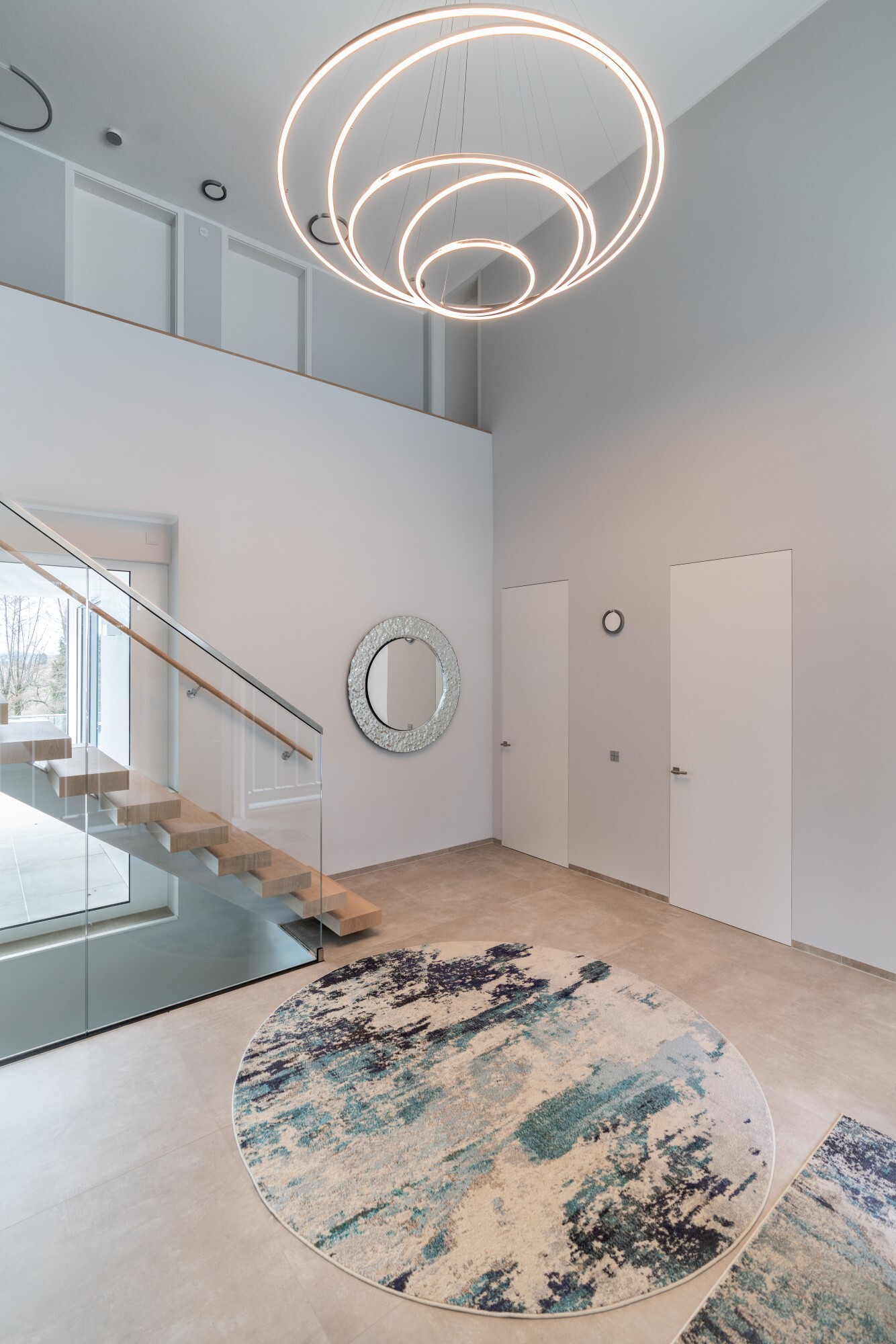 Privates Treppenhaus mit der TOCCATA - dem modernen Kronleuchter Eingangsbereich mit Treppenhaus mit gerader einläufiger Treppe eines modernen Privathauses und Fokus auf die dekorative Beleuchtung dank eines modernen Kronleuchters bestehend aus 3 Ringleuchten TOCCATA.