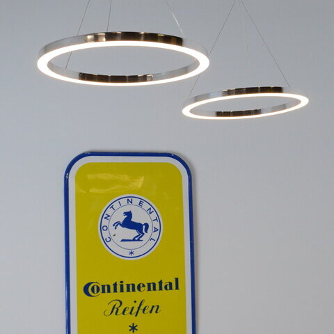 Two small polished aluminium ring lights suspended at different heights in front of a Continentale metal shield. TRIS pendant light.