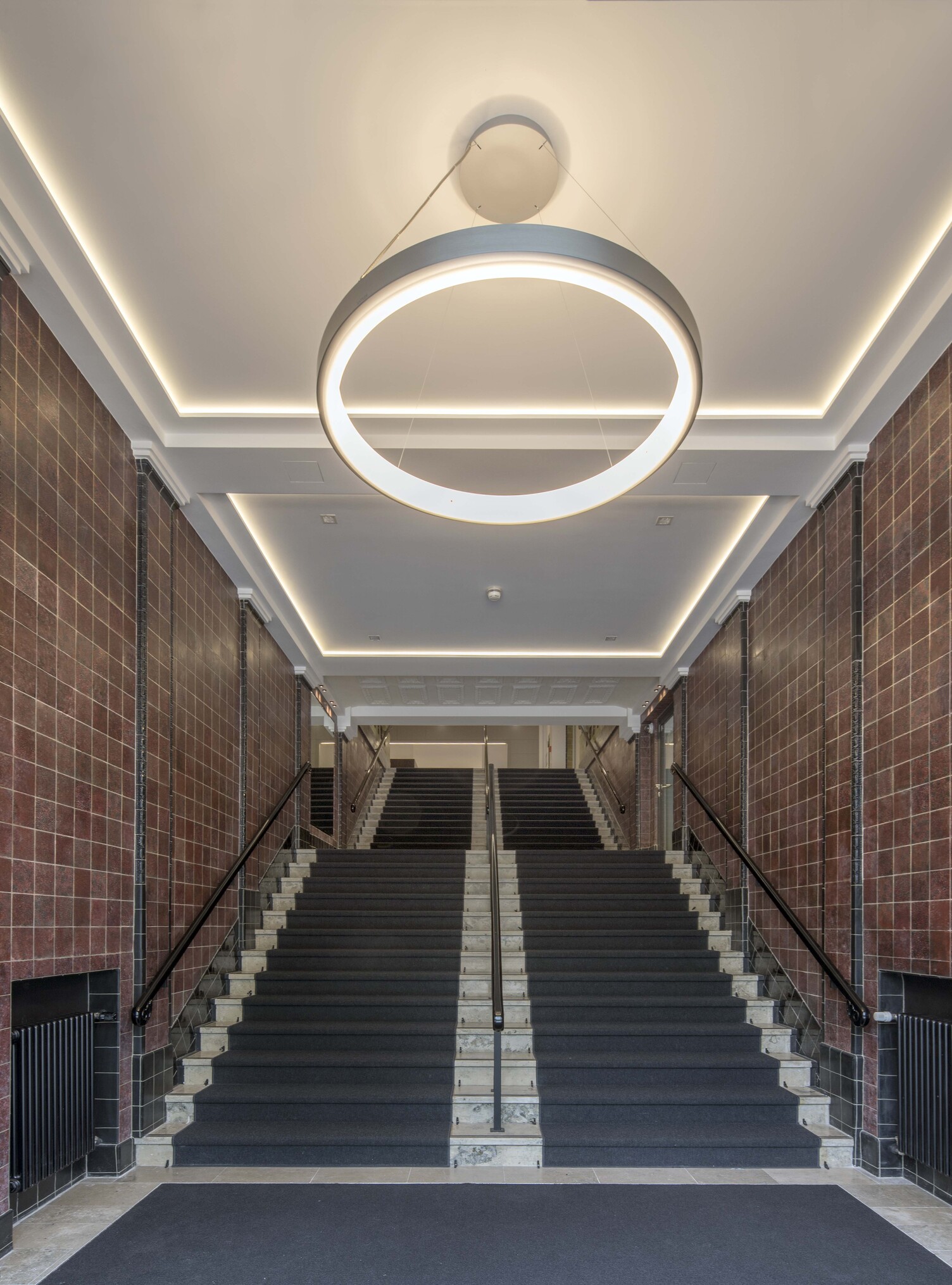 Blick auf einen Treppenaufgang mit Fokus von unten auf eine abgependelte Ringleuchte Circolo im DGB Hamburg.