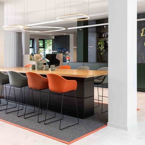 Slim Delta Direct luminaires from SATTLER on a conference counter Meeting point with Slim Delta Direct luminaires from SATTLER. In the background, a reception desk with Paladio System Track luminaire and Paladio System LENS, each installed as a pendant version at different heights. Avveni Pendant 1 and Evo Spot were also used in the Track luminaire