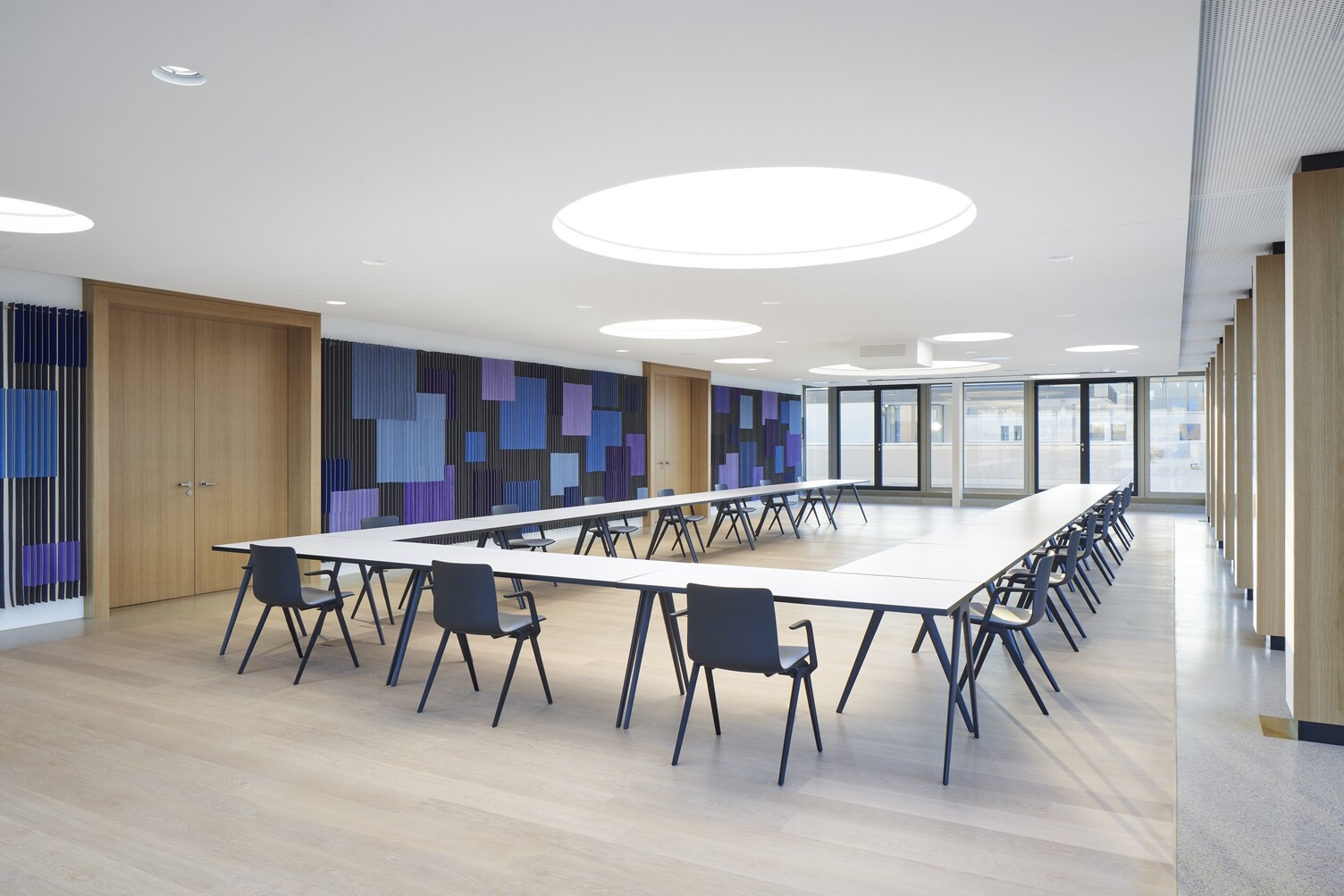 Modern conference room with round light ceilings Conference room with a large U-shaped arrangement of tables, the walls are graphically designed in shades of blue, round light ceilings are distributed around the room in the white ceiling.