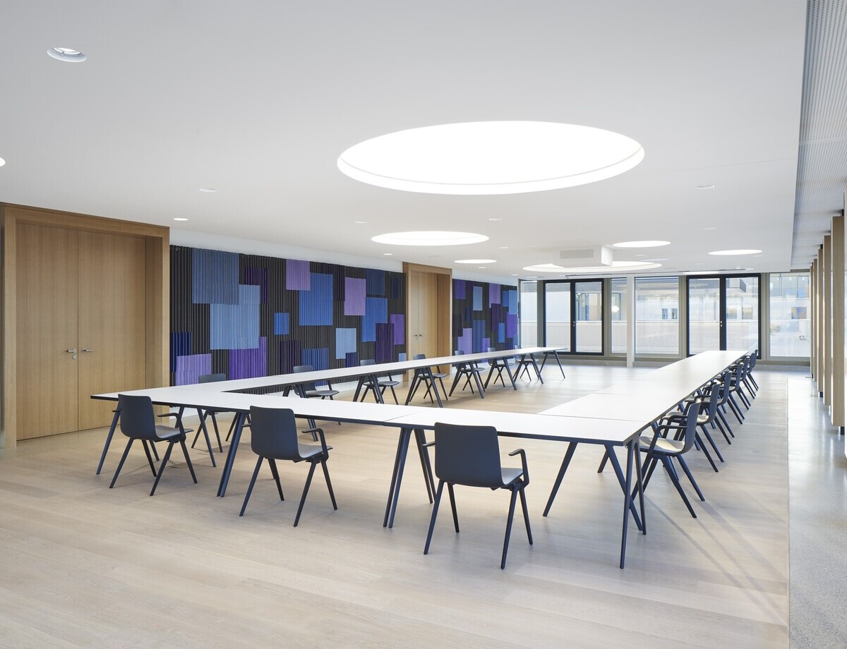 Modern conference room with round light ceilings Conference room with a large U-shaped arrangement of tables, the walls are graphically designed in shades of blue, round light ceilings are distributed around the room in the white ceiling.