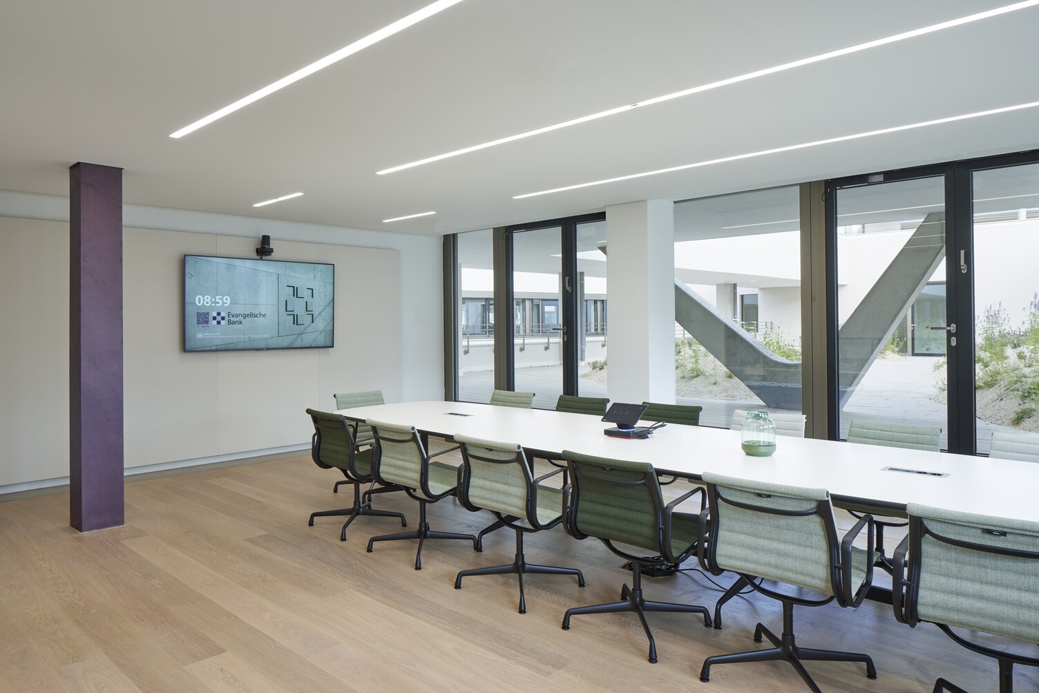 Konferenzraum der EVB mit einem ovalen Meetingtisch und Bürostühlen darum herum in der Mitte, außenherum geben Fenster den Blick nach draußen frei, in der weißen Decke sind lineare Einbauleuchten (PALADIO) sichtbar.