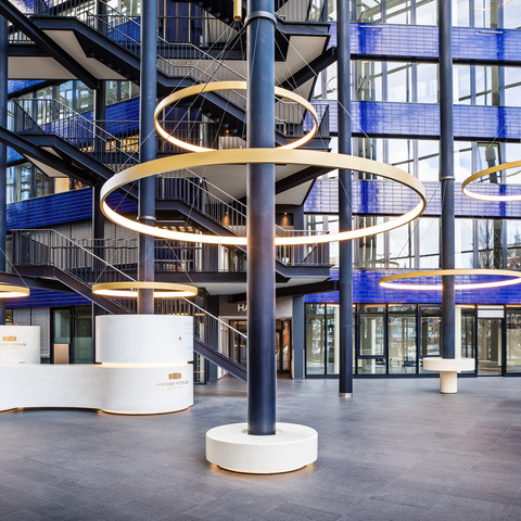 CIRCOLO ring lights around columns of the Hanseforum Hamburg atrium Golden large-format ring lights, CIRCOLO I, suspended around the columns of the glazed atrium with blue walls of the Hanseforum Hamburg.