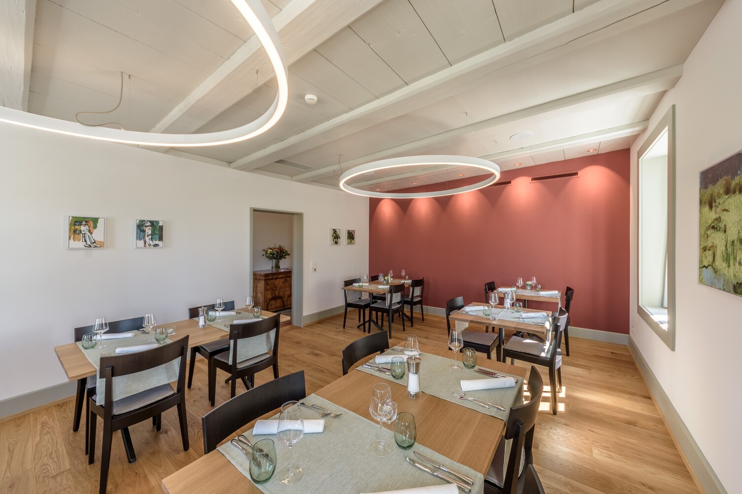 Cosy, bright restaurant room with a red wall and white DUETTO ring lights, suspended from a white wooden ceiling.