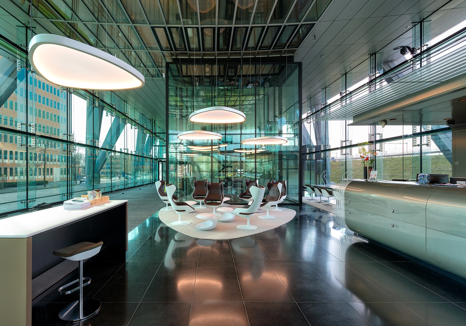 Soft Delta L+A über Sitzbereiche einer Lobby Stoffbespannte Soft Delta Light & Acoustic Leuchten von SATTLER in einer modernen gläsernen Lobby mit Empfang und Cafeteria