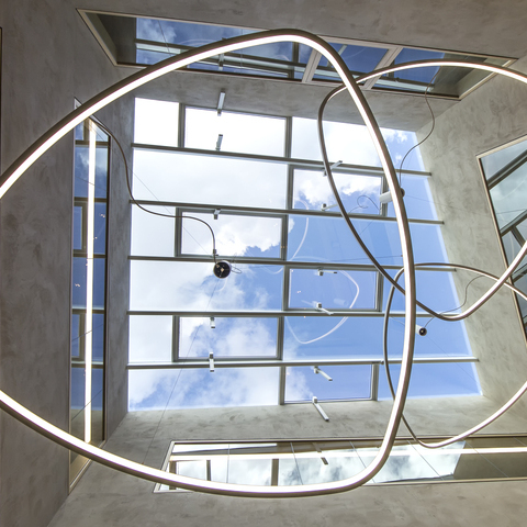 Central view from below in SATTLER SOFT DELTA I with pendulum canopy suspended under glass roof in lobby Central view under the SOFT DELTA I luminaire from SATTLER mounted on a pendant canopy under a glass roof,