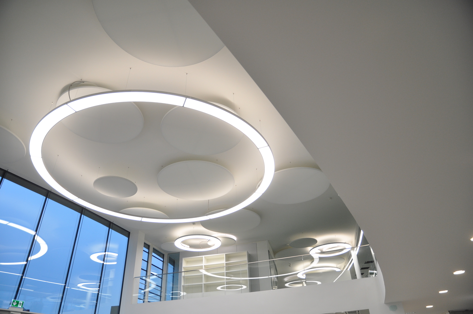 Runde Pendelleuchte Anello 6m und Acoustic Panel im Foyer der Münzing Chemie In einem Foyer mit Blick in Richtung einer 6m Anello in Aluminium poliert und parallel dazu montierten Akustik Panel jeweils von SATTLER.