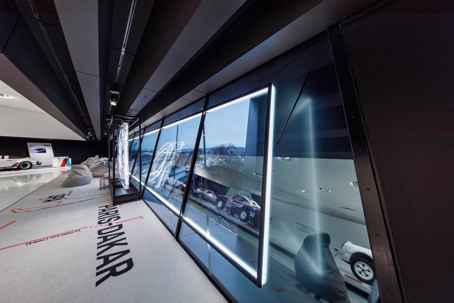 Interior view of the Porsche Museum in Stuttgart with the Paris-Dakar exhibition and modern lighting by Sattler to mark the 70th anniversary of Porsche sports cars. For the windows, an illuminated frame was planned, developed and installed as an illuminated picture frame with our CoveLighting in a special design.