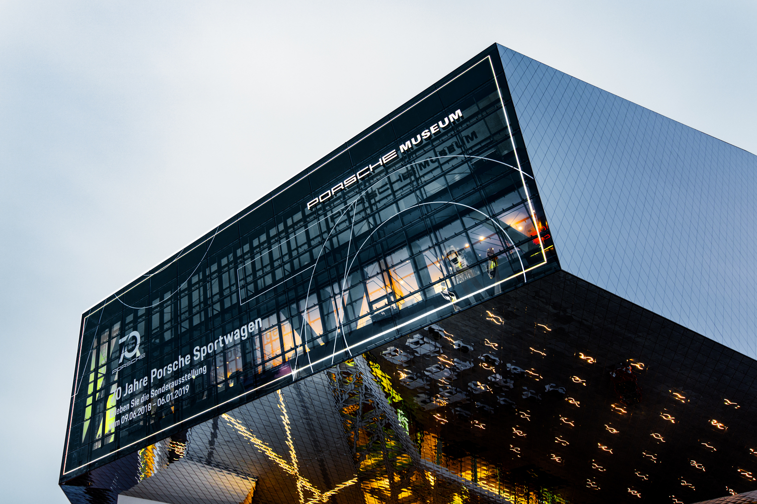 Exterior view of the Porsche Museum in Stuttgart in the evening, with Sattler's lighting illuminating the façade. A total of over 160 metres of CoveLighting elements were assembled into a large window frame and mounted on the window front for the 70th anniversary of the Porsche sports car by the company's own SATTLER installation team.