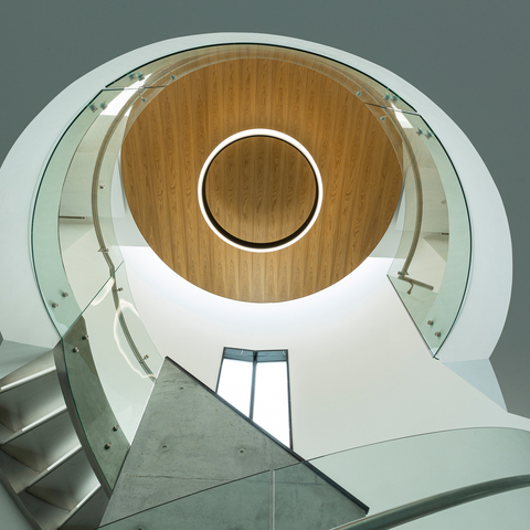 Illumination of the stairwell with large-format ring luminaires View upwards in a stairwell with a glass handrail and a round outward-radiating luminaire, CIRCOLO INVERSE (diameter 1600), in the centre of the wooden ceiling.