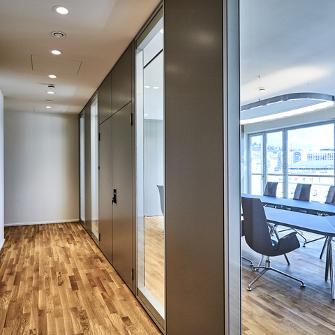 Hallway lighting | Round recessed downlights BE2 Corridor in a modern office with strip parquet flooring, illuminated by small round recessed spotlights, BE2 luminaires. Through a glass front, you can see into an adjacent meeting room with a table, chairs and rectangular SOFT SQUARE ring luminaire.