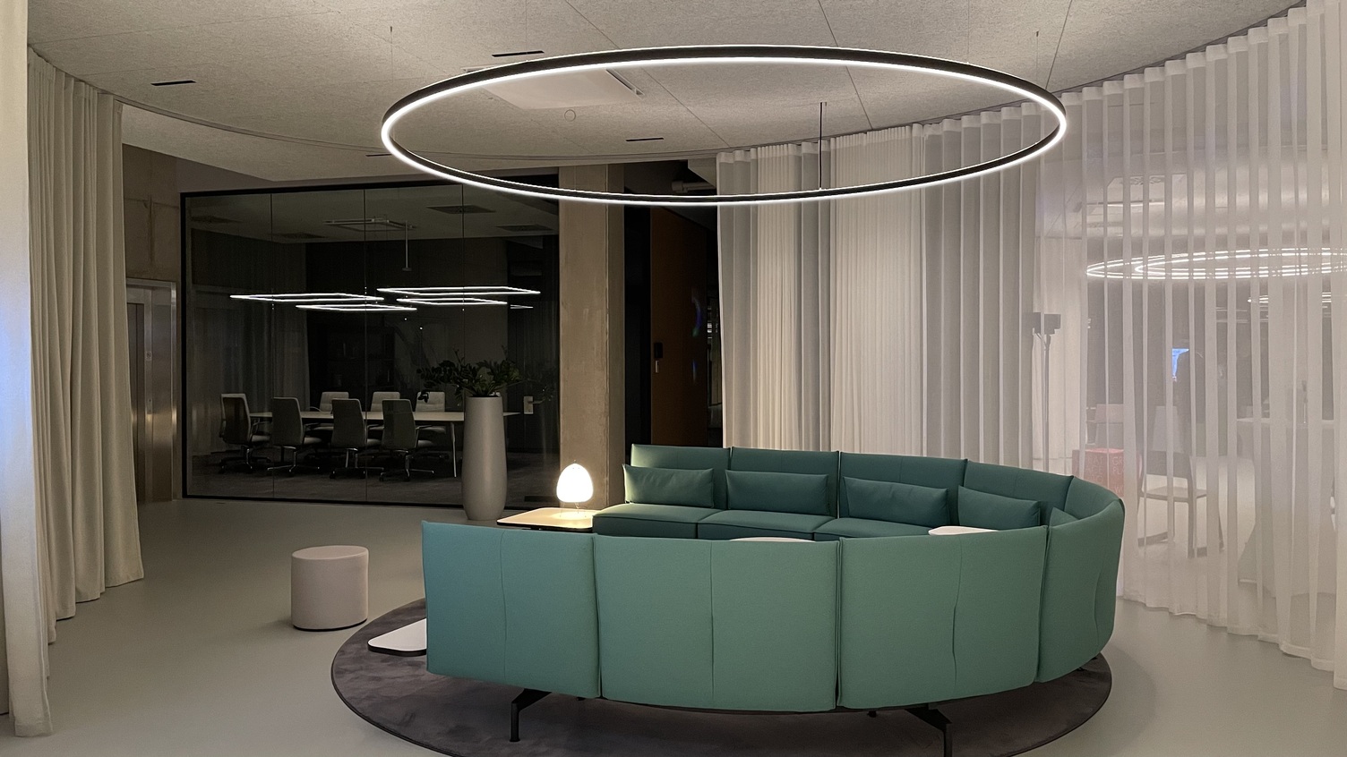 Dispute meeting area with an aesthetically shaped green U-shaped sofa - staged with Doppio by Sattler Round meeting area at Streit, featuring a central seating arrangement and Sattler's Doppio lighting fixture. In the background is another meeting island with the Gioco luminaire series