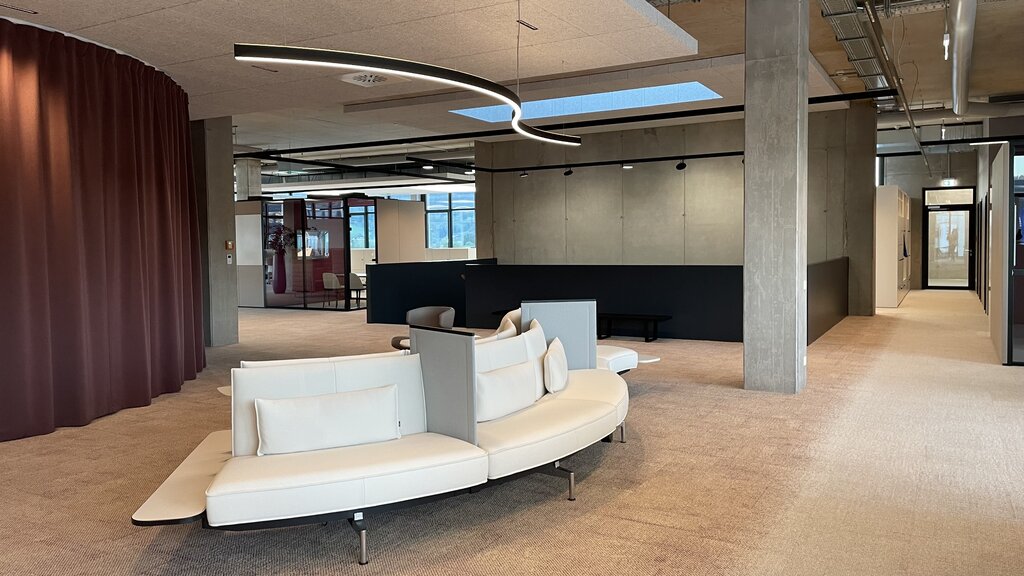 Lounge area or flexible meeting area with sofa in S-shape, above linear luminaire in the same curved shape (DUETTO).  | © Kuehnmedia