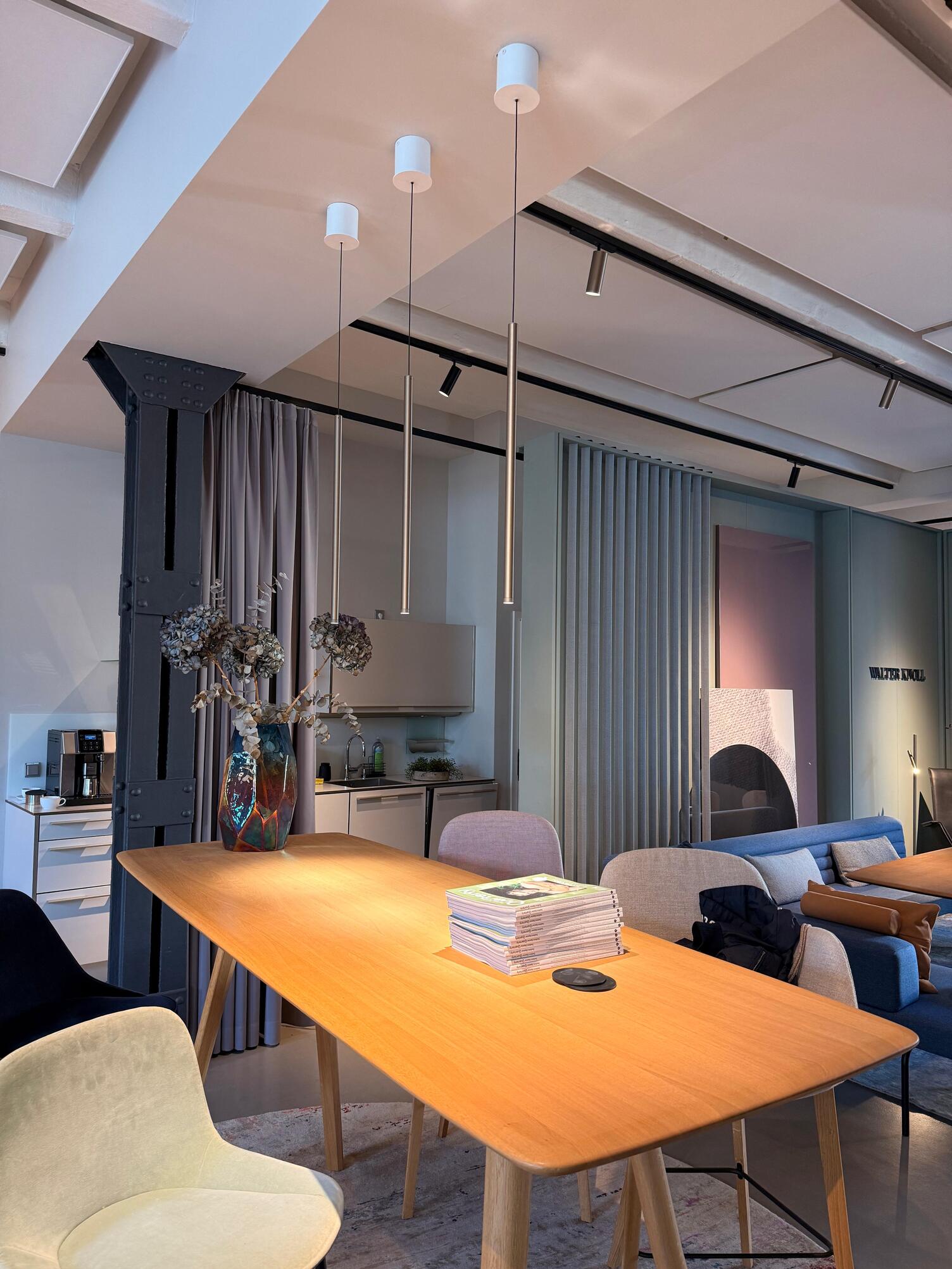 Tresen- & Hochtischleuchten: FINO, die elegante zylindrische Pendelleuchte Brauner Holzhochtisch mit Barhockern. Entlang der Länge sind drei elegante zylindrische Pendelleuchten der FINO Leuchtenserie von SATTLER abgependelt.